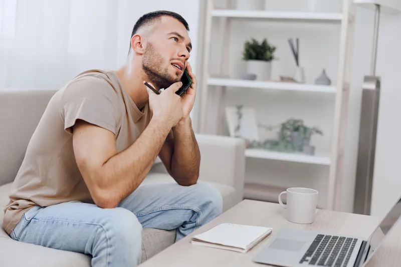 Thoughtful man on the phone in a modern home setting, showcasing productivity and communication, amid natural light and minimalist decor.