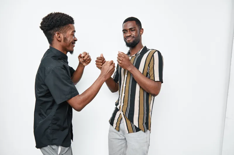 Two African American men with dark skin smiling and greeting each other with handshake and fist bump in casual clothes on white background. Friendship and connection concept.