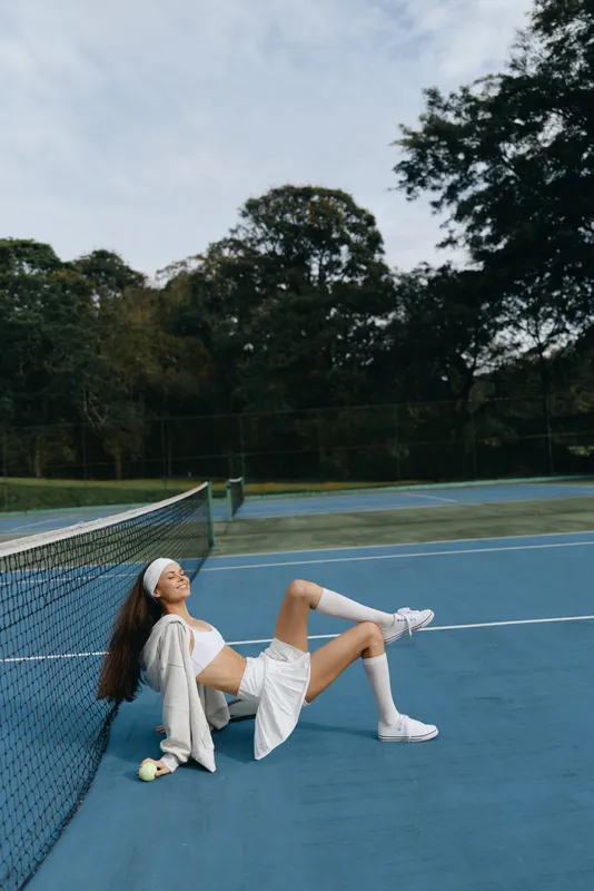 Young athletic woman in sportswear enjoying leisure time on a tennis court, exuding confidence and relaxation while posing by the net