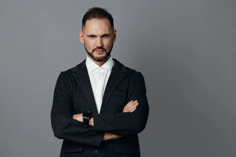 A poised business professional stands against a solid colored backdrop, exuding confidence and focus in a tailored outfit, ready for leadership tasks and strategic decision making.