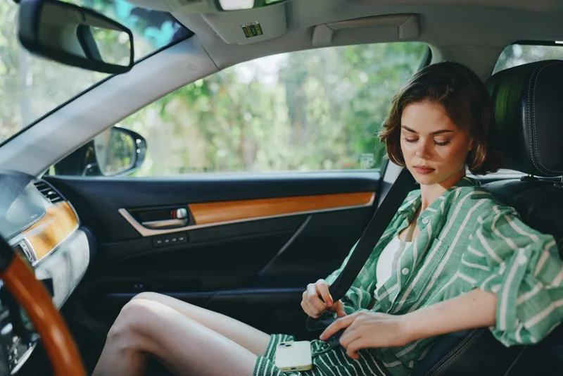 A woman sits in the driver seat of a car with a relaxed smile, hands on the wheel, ready for a journey