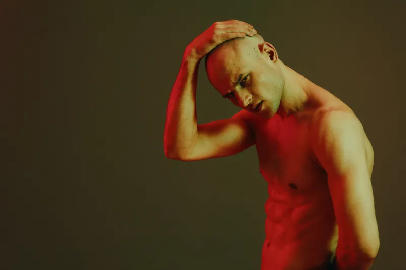 Strong man posing with a thoughtful expression, illuminated by dramatic red light against a dark background, creating a striking black and white image.