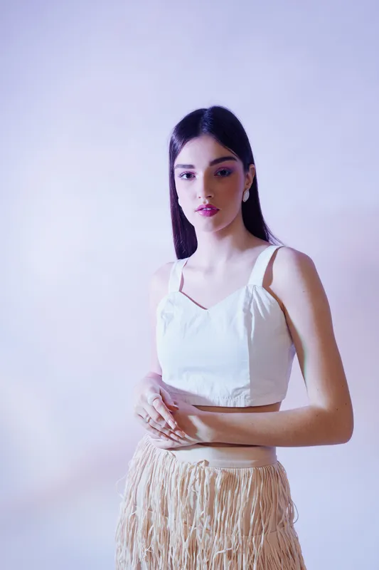 Young woman in a white top and textured skirt poses with a calm expression on a soft purple background. Concept of beauty, fashion, and elegance in studio lighting.