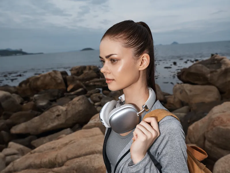 Young woman with headphones standing by the seaside, wearing activewear, showcasing a calm emotion under a cloudy sky Perfect for concepts of relaxation and outdoor activities