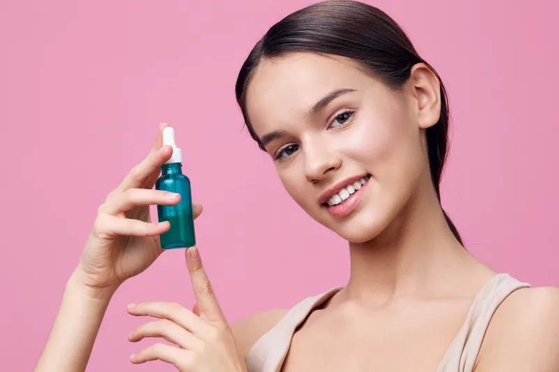 Young woman holding a skincare serum on a pink background, showcasing healthy skin and natural beauty, perfect for beauty and wellness concepts