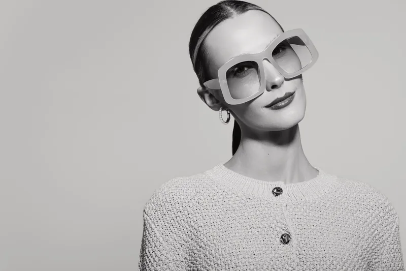 Stylish caucasian woman with fair skin wears large sunglasses and textured jacket, posing confidently against plain background. Concept of fashion, elegance, and modern style.
