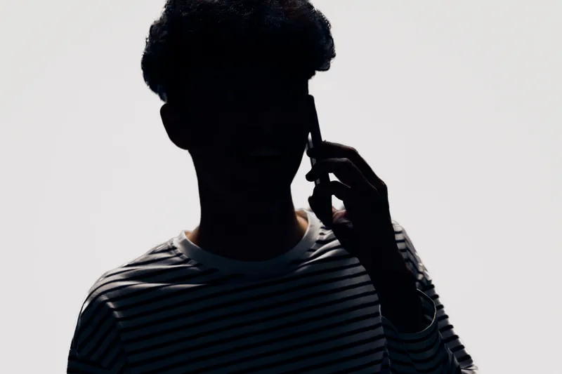 Silhouette of a young man talking on smartphone wearing striped shirt with minimalistic gray background, highlighting shadow and modern communication concept.