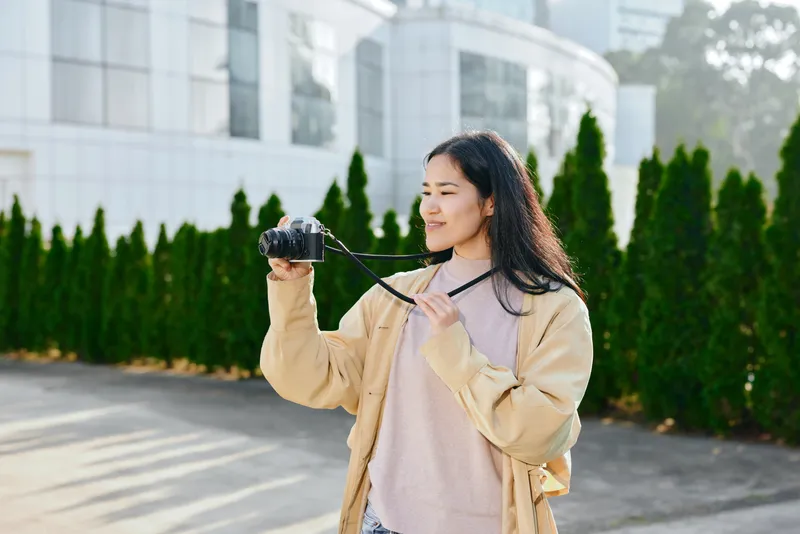Casual woman outdoors holding a camera, capturing a daylight moment, relaxed and focused, showcasing photography, lifestyle, and travel vibes with candid stance and urban scenery in a bright outdoor