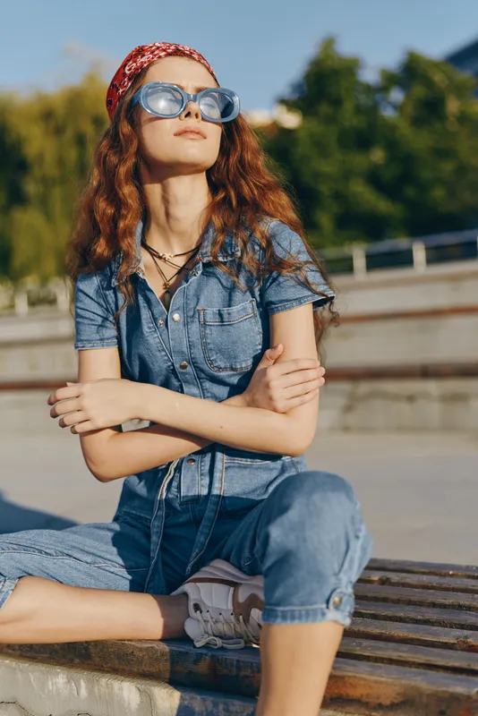 Lifestyle woman in modern boho-western denim street style wearing sunglasses and a red bandana, relaxed outdoors in warm natural light with film color tones.