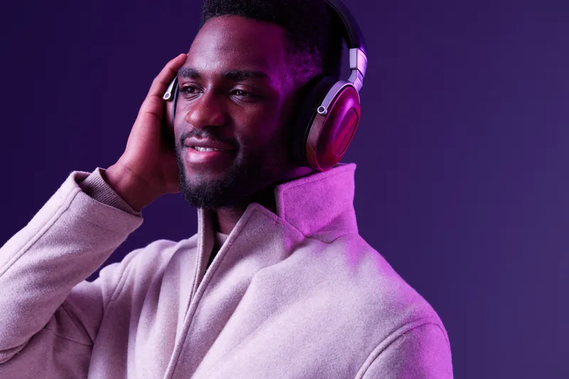 A stylish young man enjoying music with headphones, wearing a light coat, against a vibrant purple background, exuding joy and relaxation, ideal for modern lifestyle concepts