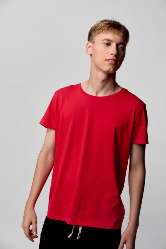 Red t-shirt worn by a young man in a casual studio setting, relaxed pose, soft lighting and plain background, highlighting simple everyday fashion and comfortable wearable style.