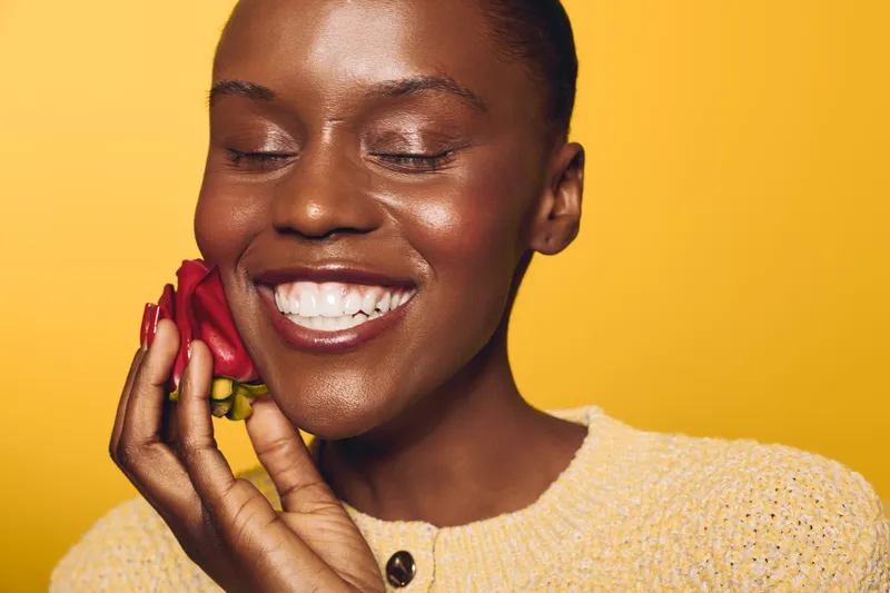 Smiling dark skinned African woman with closed eyes holds red chili pepper near face on yellow background. Concept for natural beauty, healthy lifestyle, and organic food.