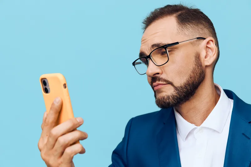 A focused business professional man checks his phone against a vibrant colored background, conveying concentration, confidence, and curiosity in a modern work moment.