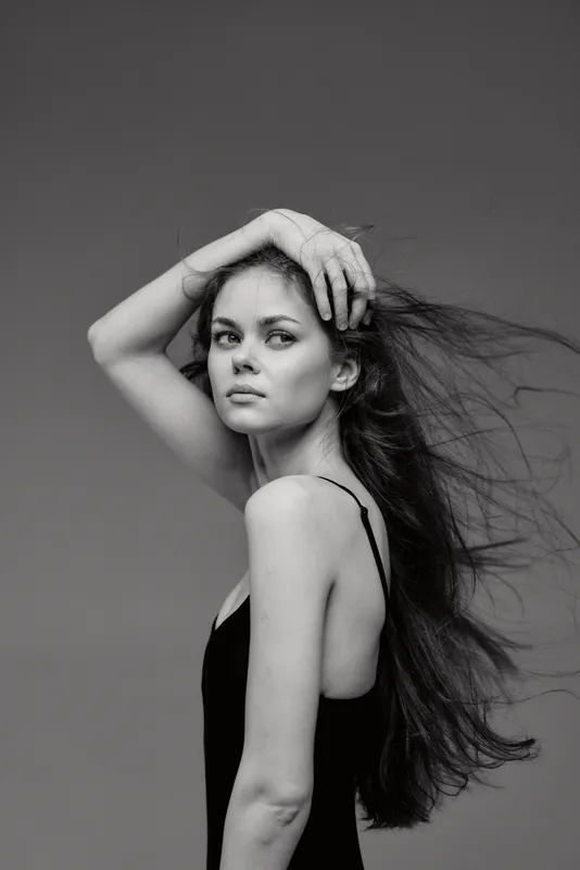 Black and white portrait of a young woman with long flowing hair and a contemplative expression against a plain background.