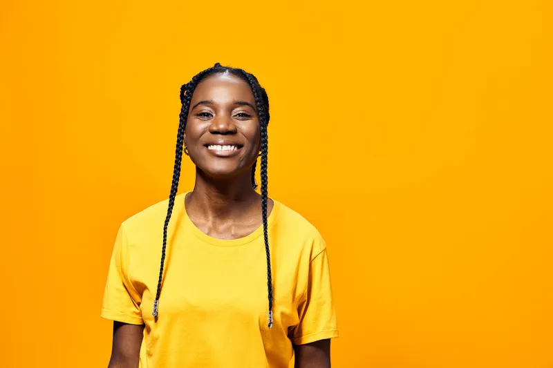 Happy young African American woman in a bright yellow t shirt smiling against a vibrant yellow background, conveying joy and positivity in a casual style