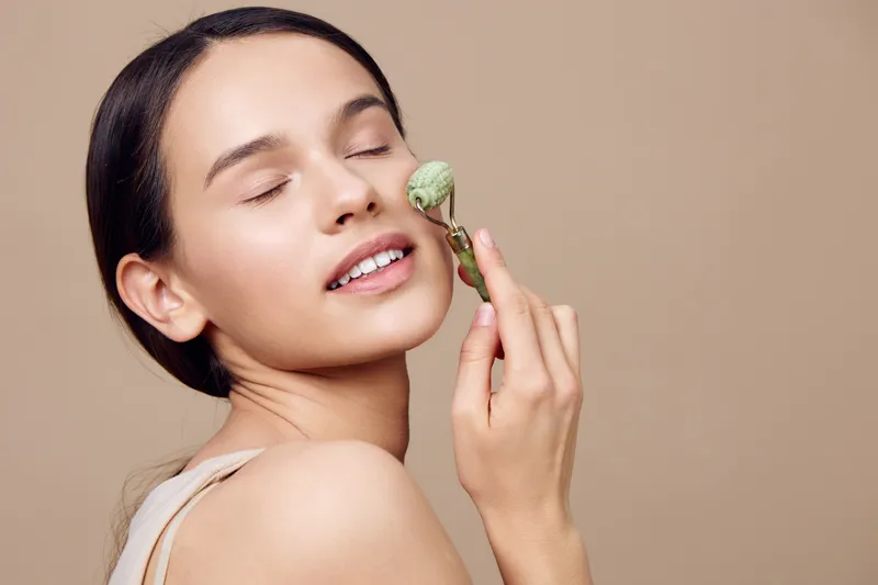 Young woman enjoying facial massage with jade roller, promoting relaxation and beauty, natural skincare routine, minimalist background