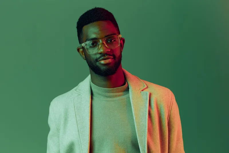 Stylish African man in glasses poses confidently against a colorful green background, showcasing modern fashion and contemporary style