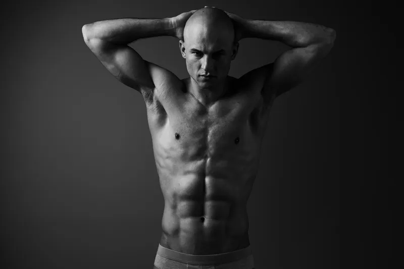 Black and white portrait of a muscular man showcasing strength, confidence, and determination with a dramatic pose in a minimalist setting.