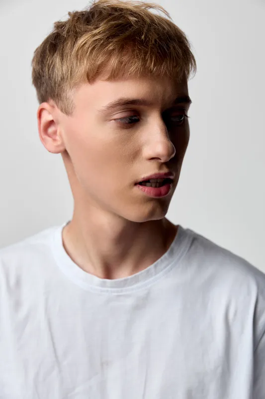 Man in a white t-shirt, studio lighting highlights a thoughtful side view profile, casual style and calm mood. Ideal for fashion, lifestyle, and editorial projects with a clean, modern feel