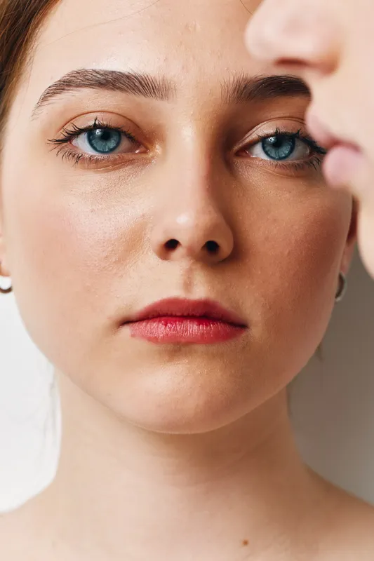 Portrait of woman face with blue eyes and red lips closeup. Natural skin texture and focused expression in soft light with blurred side profile in background.