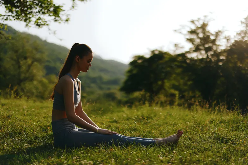 Young woman practicing yoga in nature, wearing activewear, enjoying tranquility in a serene outdoor setting, surrounded by greenery and sunlight