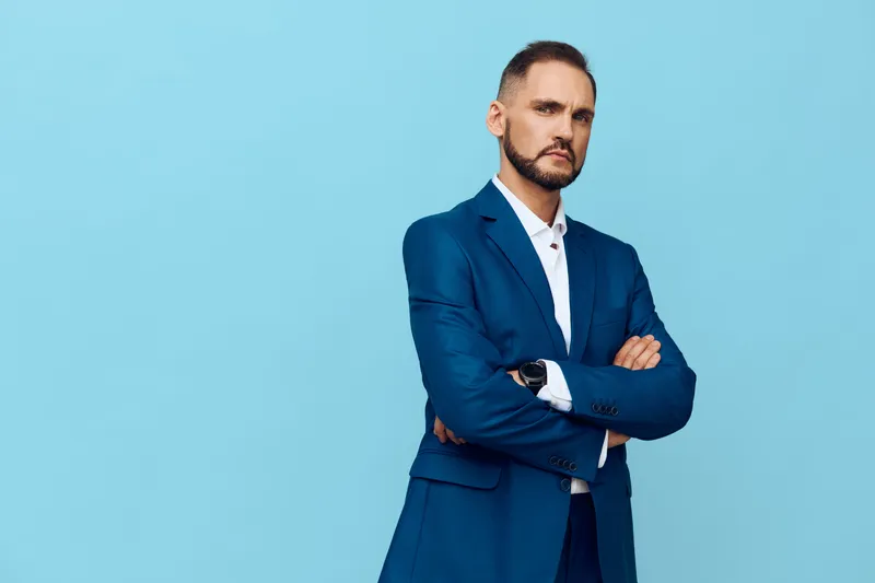 A composed male professional stands against a solid blue background, exuding confidence and focus as he crosses arms in a poised, executive stance.