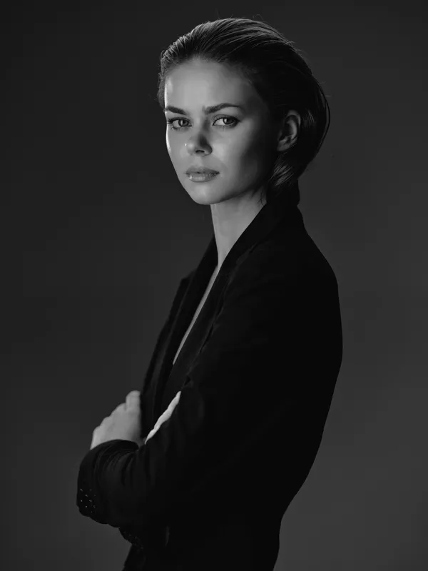 Black and white portrait of a serious woman in blazer with crossed arms, monochrome studio background, elegant confident expression