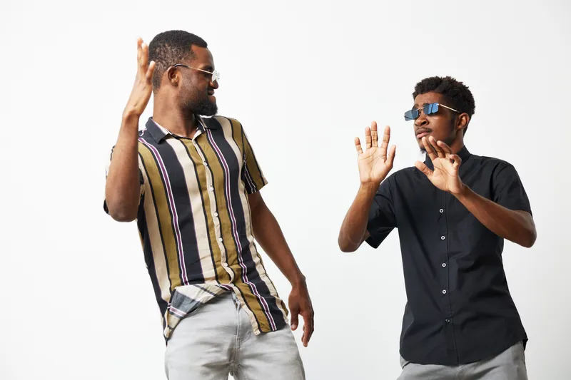 Two black men enjoying a fun moment, dressed in casual outfits. One man wears sunglasses, and they express joy and excitement together.