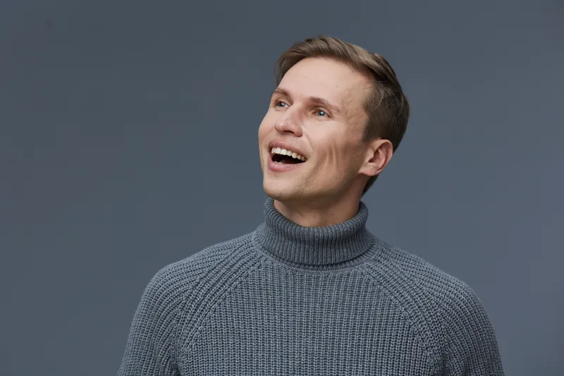 Smiling man wearing gray knitted turtleneck sweater looking away isolated on dark gray background, happy cheerful male portrait, digital nomad, freelance communication concept