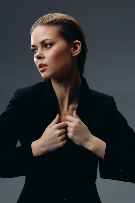 Serious woman in black suit posing against dark background, looking aside with confident expression.