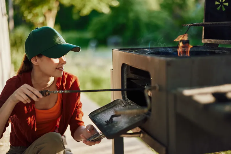 Woman grilling outdoors in a warm season, showcasing joy and relaxation in a green garden setting surrounded by nature