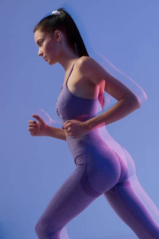 Woman sport fitness in purple seamless activewear running indoors with dynamic motion blur on blue background, showcasing strength and endurance for healthy lifestyle.
