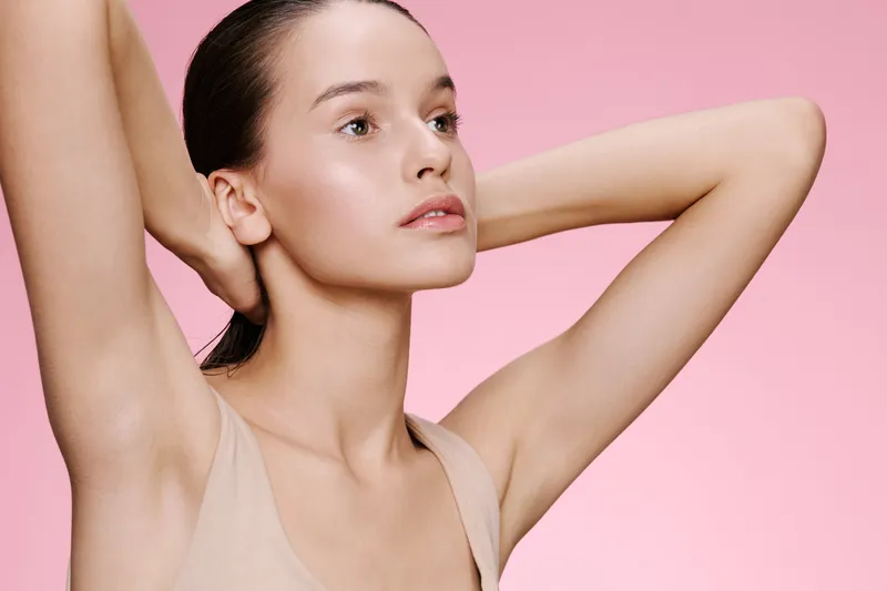 Portrait of a young female model with a serene expression, showcasing healthy skin against a soft pink background, ideal for beauty and skincare themes