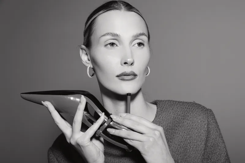 Portrait of a fair skinned Caucasian woman holding a high heel shoe near her face in studio lighting.