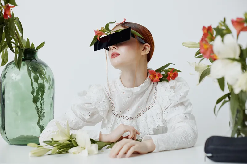 Stylish woman with unique glasses and flowers, showcasing contemporary fashion and emotions of tranquility in a minimalist setting