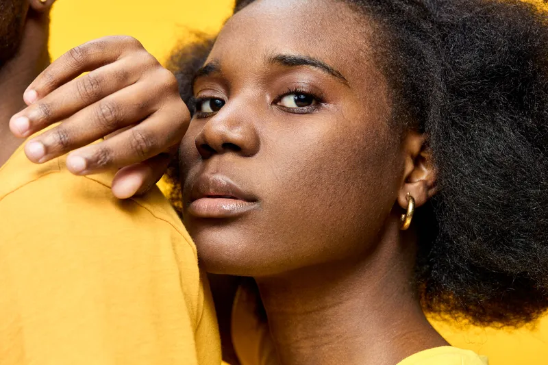 Portrait of a young Black woman with natural hair, wearing a yellow shirt, showcasing confidence against a vibrant yellow background with a fresh and energetic vibe