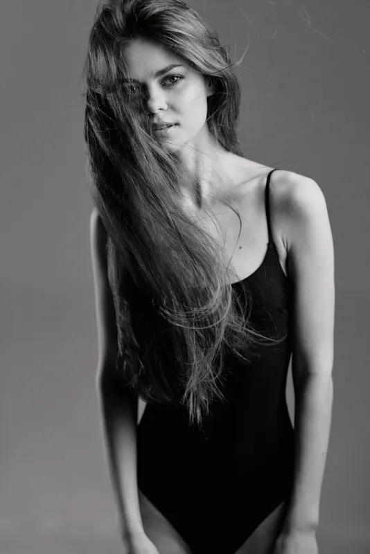 Black and white portrait of a young woman in a black bodysuit with flowing hair and a serious expression