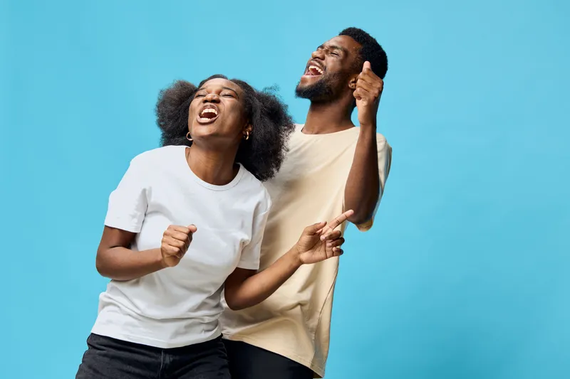 Happy diverse couple dancing joyfully against a bright blue background, showcasing vibrant emotions, stylish outfits, and a carefree attitude