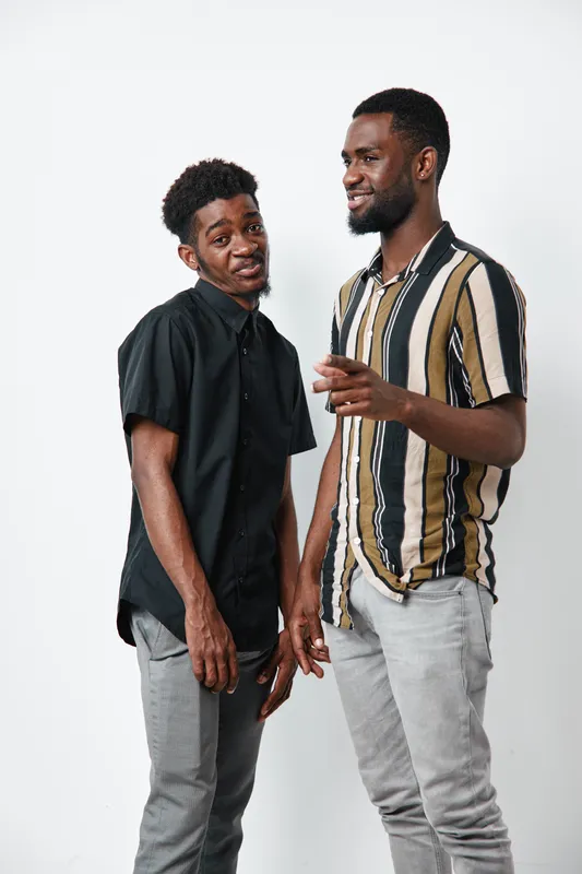 Two young black men with dark skin standing and smiling together in casual clothes on white background. Male friends, communication, happiness and positive mood in studio.