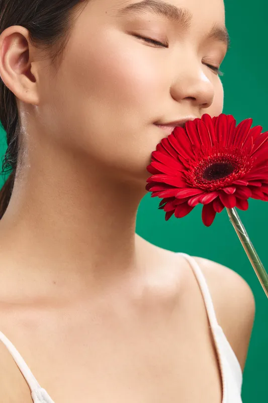 asian woman is captured in a studio portrait as she gently holds a vivid red flower near her face, soft lighting and gentle expression creating a calm, elegant mood.