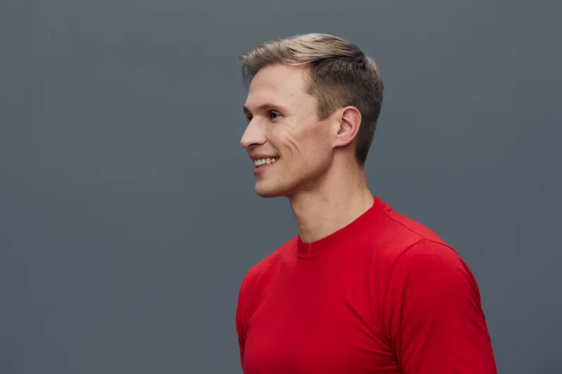 Smiling man wearing red casual t-shirt looking to the side against plain gray background. Studio portrait capturing happiness, positive emotion, and relaxed style with natural lighting and simple comp