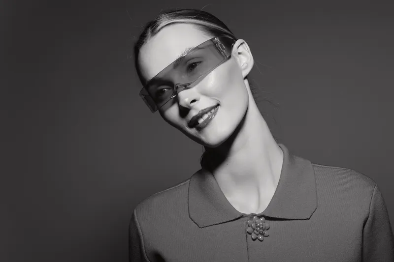 Portrait of a smiling young caucasian woman with pale skin wearing transparent sunglasses and textured shirt. Studio shot in black and white.