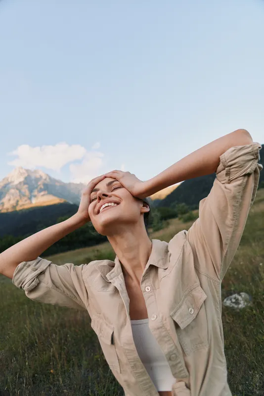 Happy woman in beige shirt enjoying nature with mountains and blue sky in the background. Concept of lifestyle, freedom, and outdoor relaxation.