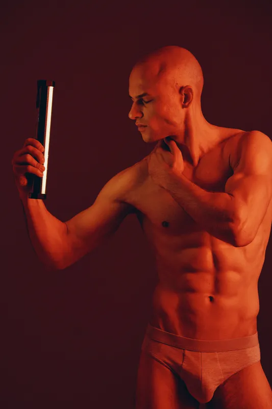 Strong man posing with a light source against a vibrant background, showcasing physique and confidence. A powerful black and white image highlighting strength and emotion.