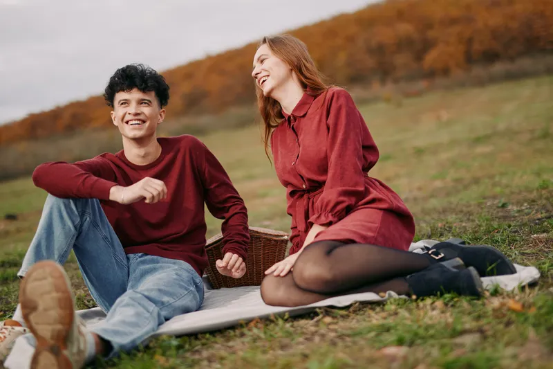 Candid outdoor picnic portrait of a young couple sharing a genuine smile and relaxed conversation on a blanket, natural clothing and believable interaction capturing true, heartfelt emotion.