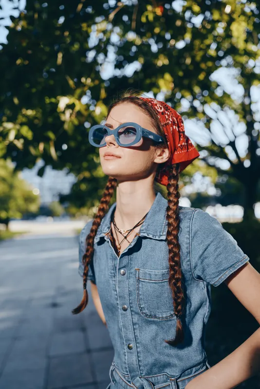 Lifestyle woman in modern boho-western denim street style wearing oversized blue sunglasses and red bandana, capturing a vibrant summer film color mood outdoors.