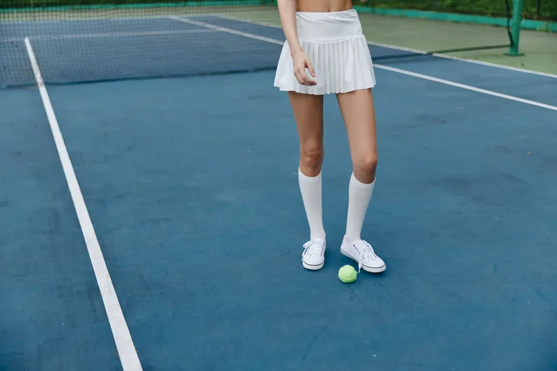 Young female tennis player in a white skirt and socks on a blue tennis court, showcasing athleticism and concentration while holding a tennis ball