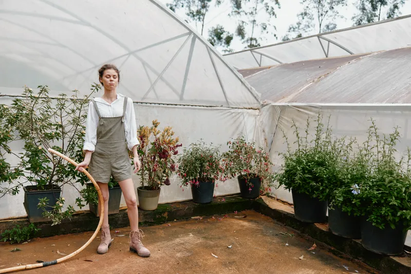 Young woman in overalls watering plants in a greenhouse, showcasing a connection to nature and sustainable gardening practices