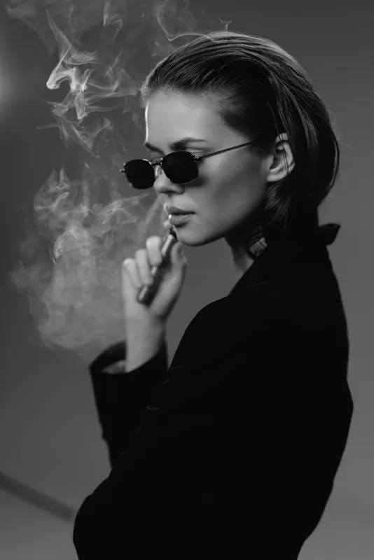 Black and white portrait of a woman smoking with sunglasses and smoke around her face.