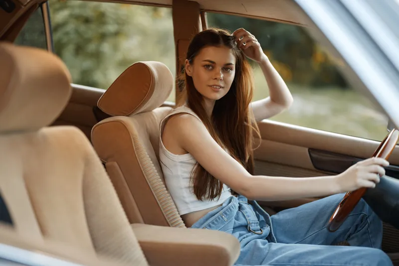 Young woman in casual outfit sitting in a vintage car, showcasing relaxed emotions and natural beauty, perfect for lifestyle and travel themes.